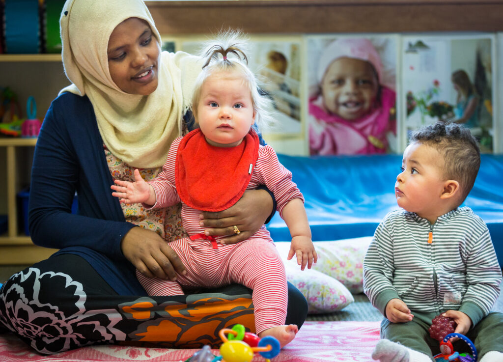 A provider holds one child while sitting next to another child